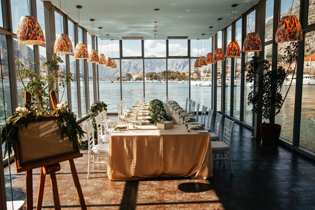 Lange Hochzeitstafel in einem lichtdurchfluteten Glaspavillon mit Seeblick als Location für eine kleine Hochzeit