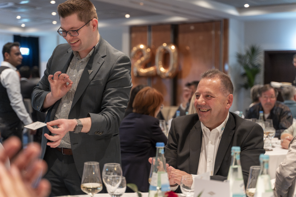 Zauberer Sven Wengerter am Tisch vor goldenen Ballons mit der Zahl 20 beim Firmenjubiläum