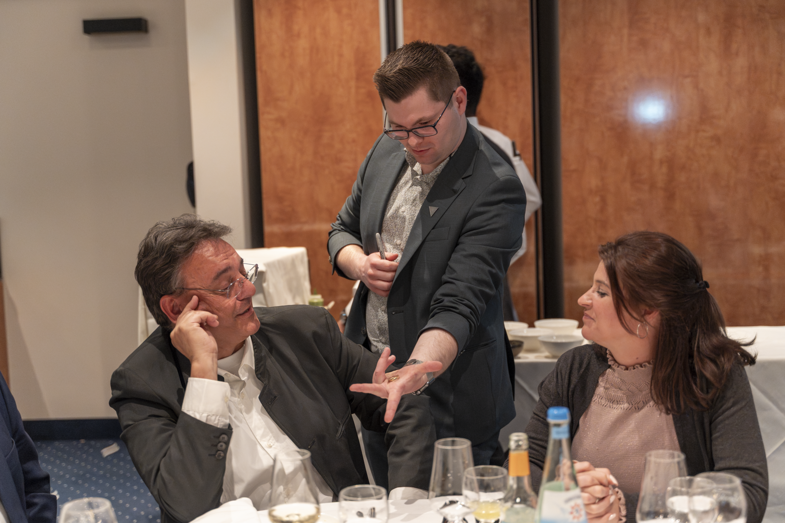 Kunden staunen bei Close-up-Zauberei am Tisch während eines Firmenevents