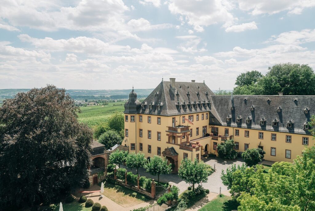 Schloss Vollrads im Rheingau aus der Vogelperspektive mit Weinbergen im Hintergrund
