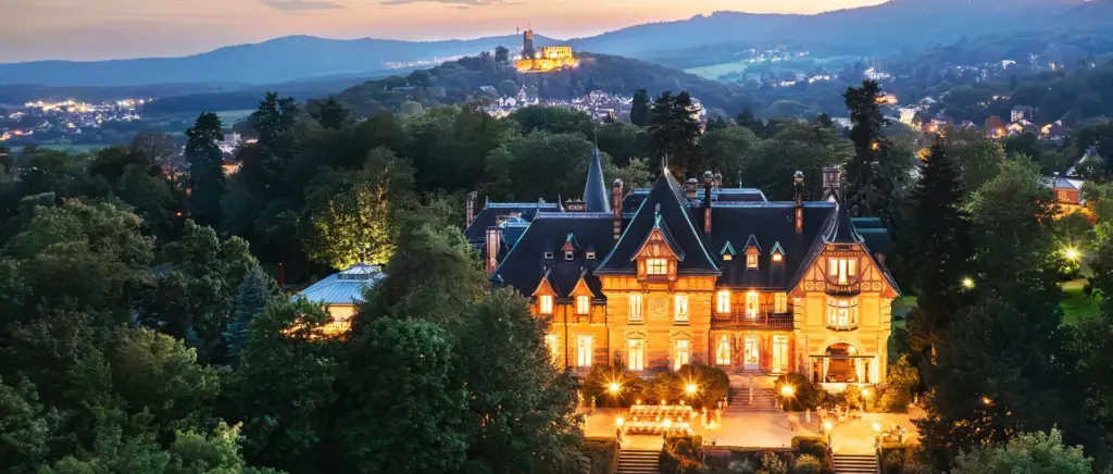 Villa Rothschild in Königstein im Taunus in der Abenddämmerung mit beleuchteter Terrasse und Burg Königstein im Hintergrund