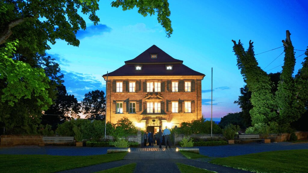 Schloss Atzelsberg bei Erlangen am Abend, beleuchtet, mit Gästen am Eingang